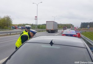 Zdjęcie kolorowe. Policjanci ruchu drogowego stoją przy kontrolowanym samochodzie BMW i rozmawiają z kierującym.