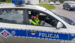 Zdjęcie kolorowe. Policjant ruchu drogowego i policjant z Samodzielnego Pododdziału Prewencji Policji siedzą w radiowozie, sprawdzają dane kierującego i sporządzają dokumentację.
