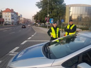 Dwóch policjantów stoi przy drodze i pilnuje bezpieczeństwa uczestników Winobrania