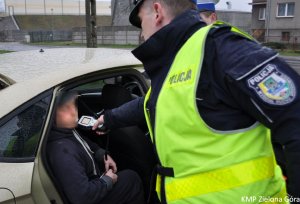 Policjant dokonuje pomiaru stanu trzeźwości mężczyzny siedzącego na tylnym siedzeniu