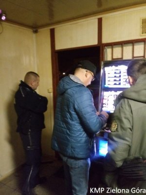 Policjant i funkcjonariusze Krajowej Administracji Skarbowej stoją przy zabezpieczonym automacie do gier