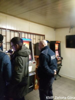Policjant i funkcjonariusze Krajowej Administracji Skarbowej stoją przy zabezpieczonych automatach do gier