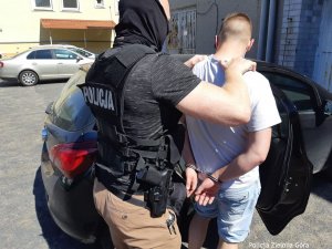 Aresztowany mężczyzna zakuty kajdankami  przez Policjanta prowadzony do radiowozu