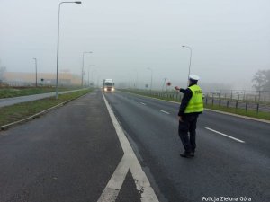 Policjant stojący na drodze i kierujący białą ciężarówkę do kontroli drogowej