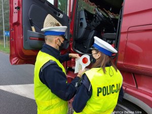 Dwóch umundurowanych funkcjonariuszy dokonuje kontroli dokumentów czerwonej ciężarówki