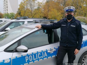 Policjant stoi obok radiowozu, rękę trzyma na dachu samochodu