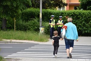 Dwoje policjantów obserwujących przejście dla pieszych, po którym przechodzi matka z dzieckiem